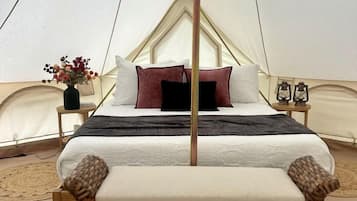 A bed in a tent with a canopy, a wicker chair, a small table with a vase of flowers, and a lantern on a bedside table.
