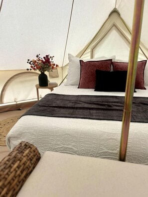 A tent-style room with a bed, pillows, a bedside table, and a vase with flowers.