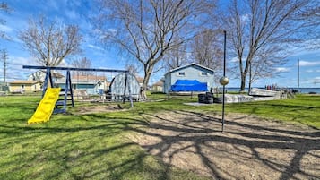 A park with a swing set, a covered play structure, and a house in the background.