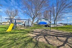 Een park met een schommel, een overdekte speelconstructie en een huis op de achtergrond.
