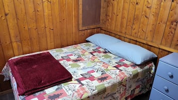 Una habitación con paneles de madera, una cama, un cojín azul y una colcha roja.