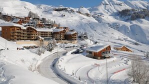 Una località turistica montana innevata con diversi edifici in legno, una strada tortuosa e un cielo azzurro limpido.