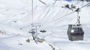 Una poltrona della seggiovia sospesa da funi con montagne innevate sullo sfondo.