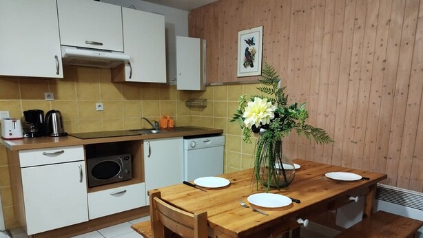 Una cucina compatta con mobili bianchi, un forno a microonde e un lavello. C'è un tavolo da pranzo in legno con piatti bianchi e un vaso di fiori.