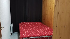 Una piccola camera con un letto singolo e una coperta a novero rossa, una parete in legno e una tenda nera.