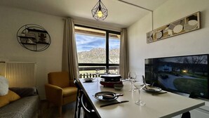 Una sala de estar moderna con comedor, televisión y vistas a las montañas a través del ventanal.