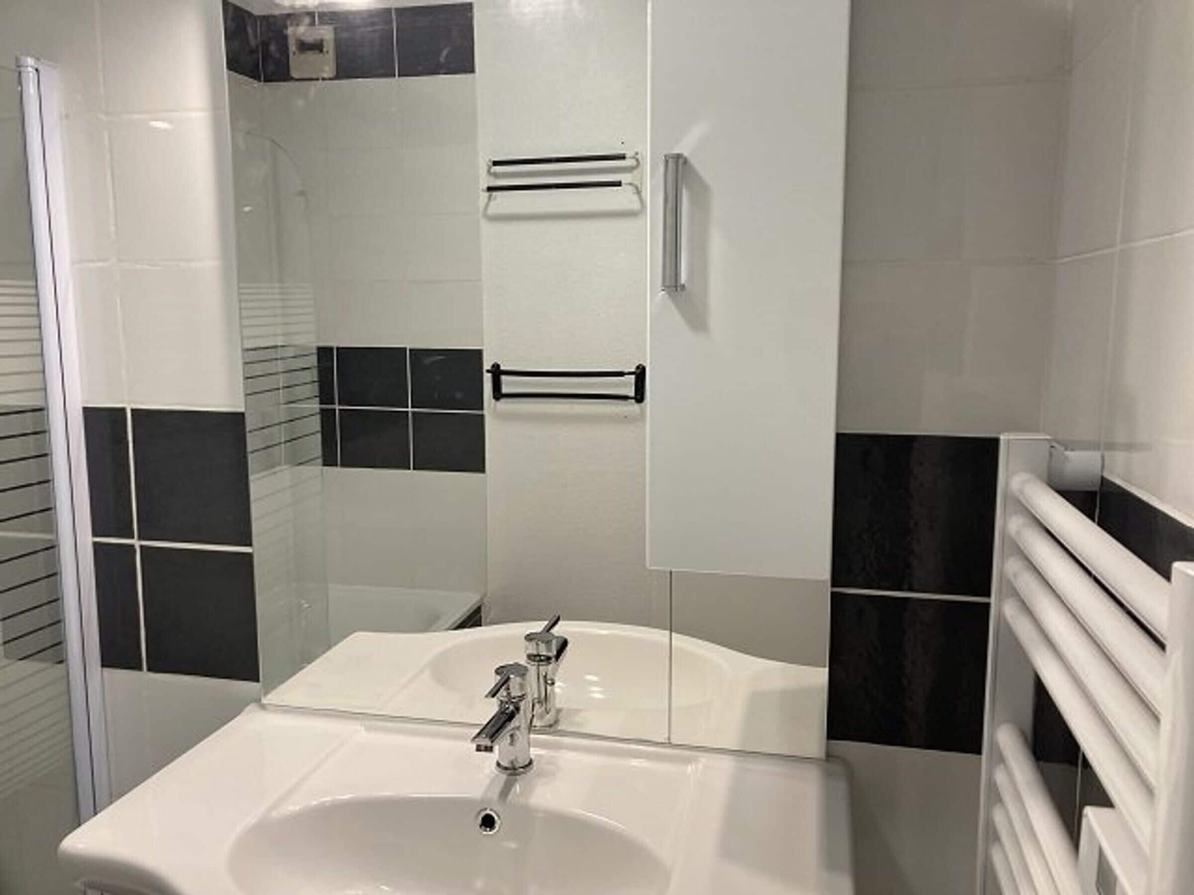 A bathroom with a white sink, a glass shower enclosure, and black and white tiled walls.