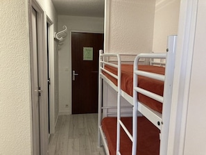 A narrow hallway with a door at the end, a white metal bunk bed with brown bedding, and a white wall. - Bright apartment near slopes - 8 guests (Orcières Merlette)