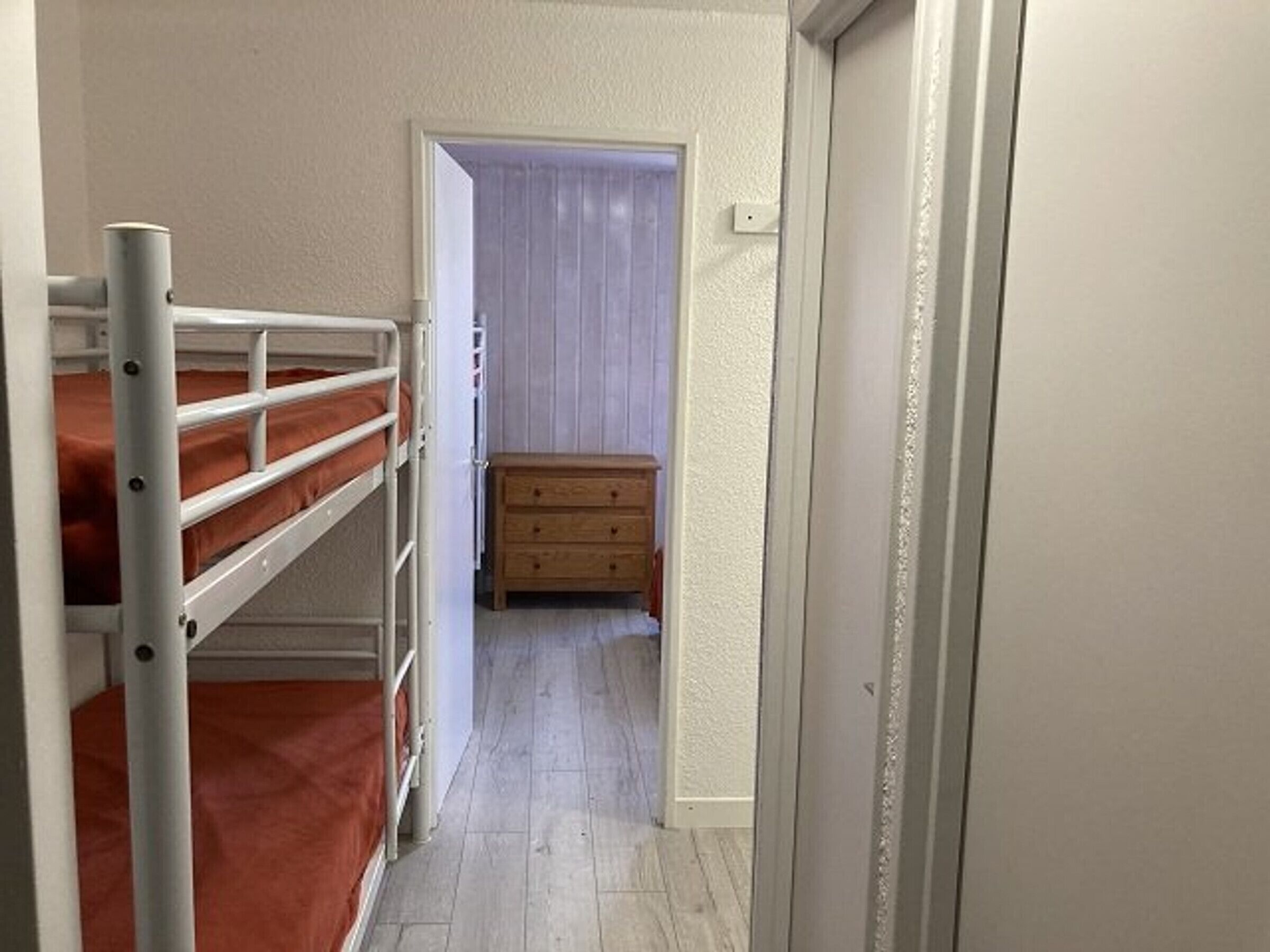 Un couloir étroit, avec des lits superposés sur le côté gauche et une commode en bois au centre.