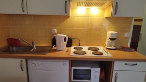 Eine kompakte Küche mit Geschirrspüler, Mikrowelle, Wasserkocher und Kaffeemaschine.