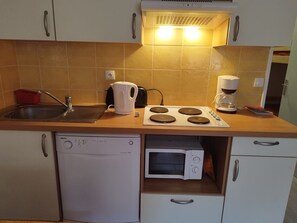 Eine kompakte Küche mit Geschirrspüler, Mikrowelle, Wasserkocher und Kaffeemaschine.