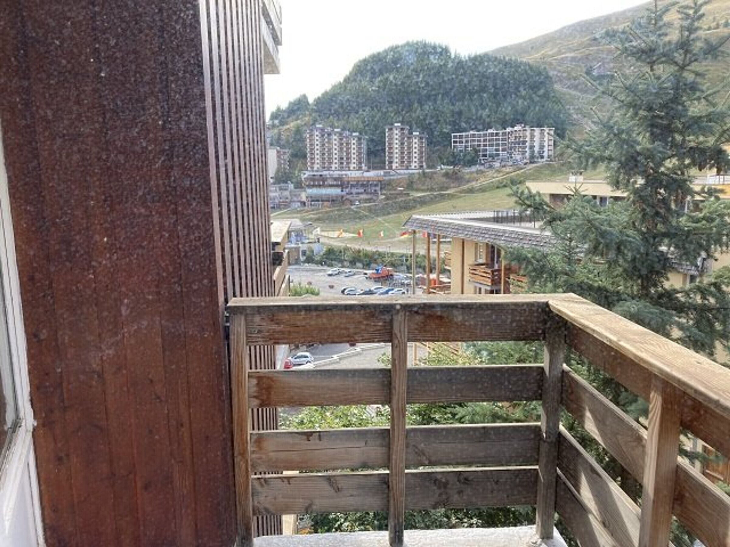 Holzgeländer eines Balkons mit Blick auf einen Parkplatz und Gebäude im Hintergrund.