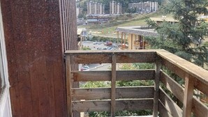 Holzgeländer eines Balkons mit Blick auf einen Parkplatz und Gebäude im Hintergrund.
