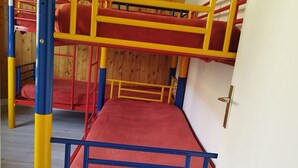 Ein Stockbett mit roter Matratze und einem blauen und gelben Rahmen, Holzwände und einer weißen Tür.