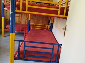 Ein Stockbett mit roter Matratze und einem blauen und gelben Rahmen, Holzwände und einer weißen Tür.