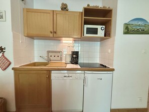 Eine kleine Küche mit Holzausstattung, einer Mikrowelle, einem Toaster, einer Kaffeemaschine und einem Geschirrspüler.