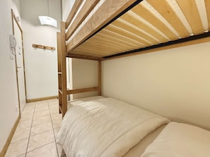 Ein Etagenbett mit Holzrahmen und weißer Bettwäsche, ein Fliesenboden und eine weiße Tür mit einem daran hängenden Handtuch.