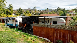 A caravan park with multiple caravans, a wooden fence, and a mountainous backdrop. - Vintage-Inspired Retro RV with Flamingo Theme Near Coast & Hiking Trails, El Cajon CA (El Cajon)