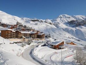 A snow-covered mountain resort with multiple wooden buildings, a winding road, and a clear blue sky. - Charming T2 with WIFI, at the ski slopes - 6 guests (Orcières Merlette)