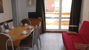 Ein Essbereich mit Holztisch und Metallstühlen, einem roten Sofa sowie einem Fernseher auf einem Holzschrank.