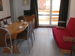 A dining area with a wooden table and metal chairs, a red sofa, and a television on a wooden cabinet. - Charming T2 with WIFI, at the ski slopes - 6 guests (Orcières Merlette)