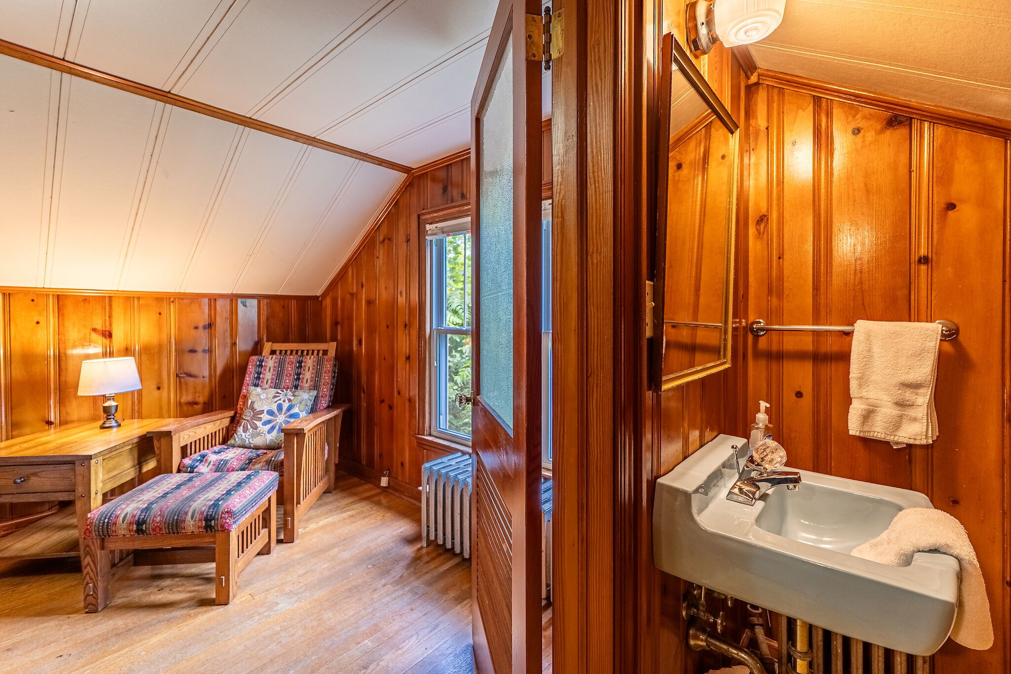 A wooden interior with a bench, a table, a radiator, and a sink with a towel.
