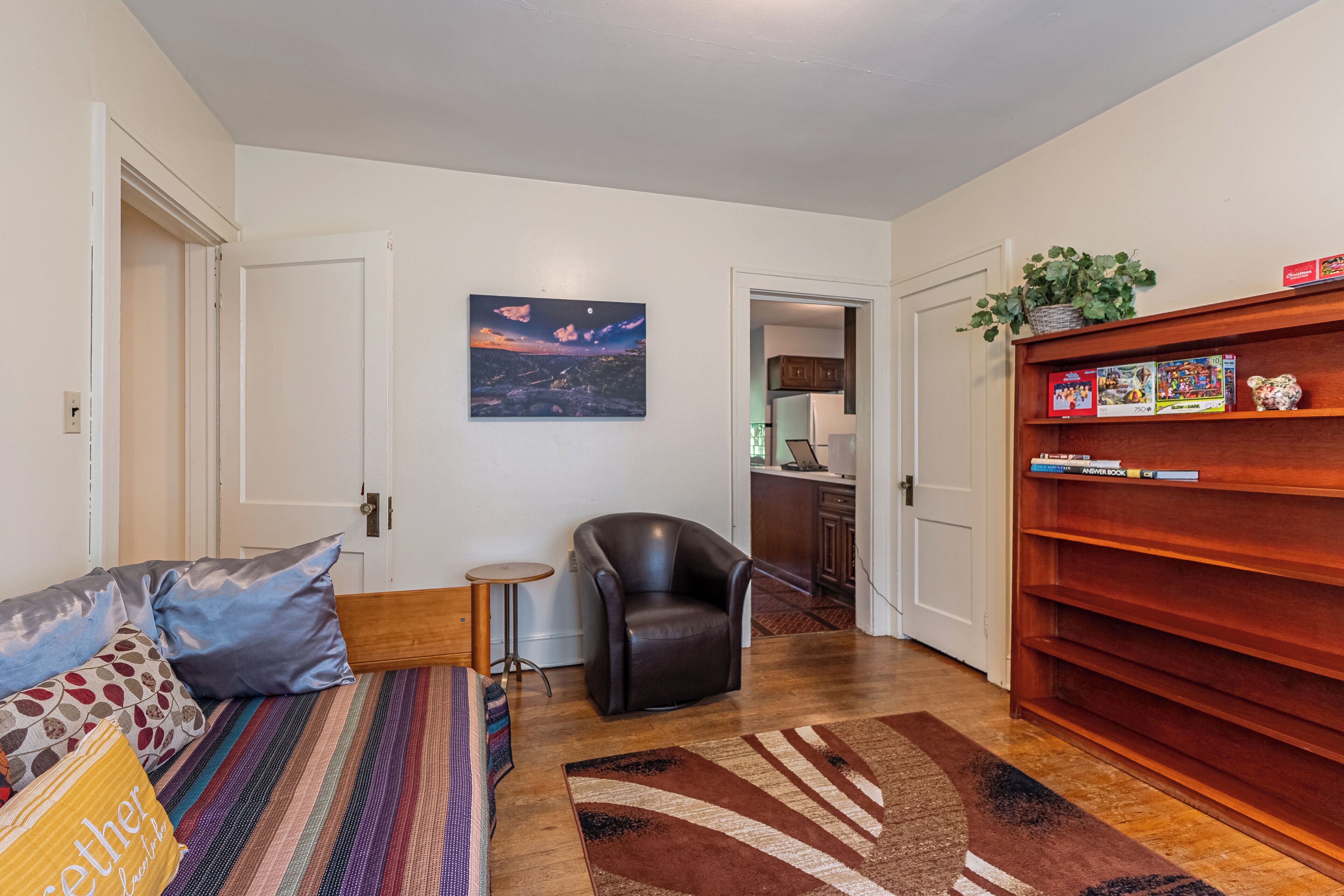 A living room with a sofa, a chair, a small table, a bookshelf, and a painting on the wall.