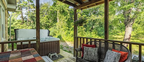 Een overdekt terras met een bank, een jacuzzi en uitzicht op een weelderige tuin.