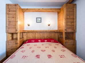 A bedroom with a wooden headboard, a bed with a red and white patterned bedspread, and two wall-mounted light fixtures. - Spacious apartment - 6 guests (La Toussuire)