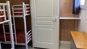 Ein Schlafraum mit Etagenbetten, einer weißen Tür, Holzwänden und einem kleinen Holztisch.