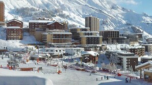 Eine schneebedeckte Stadt mit verschiedenen Gebäuden, darunter Hotels und Apartments, und eine Skipiste im Vordergrund.