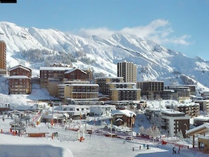 Un pueblo cubierto de nieve con diversos edificios, entre ellos hoteles y apartamentos, y una pista de esquí en primer plano.