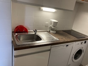 Una cocina con un lavamanos de acero inoxidable, una cafetera y una lavadora.