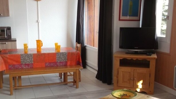 A dining area with a table covered in a patterned tablecloth, a television on a wooden stand, and a small table with a bowl. - Bright apartment near slopes - 8 guests (Orcières Merlette)