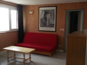Ein Zimmer mit einem roten Sofa, einem Holztisch und einem gerahmten Bild an der Wand.