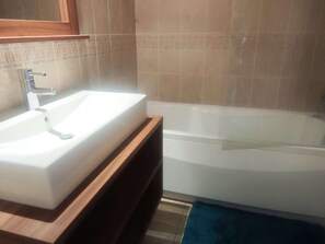 A bathroom with a white sink, a wooden vanity, a bathtub, and beige tiled walls. - Cozy apartment, slopes view - 4 guests (Isola 2000)