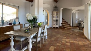 A dining area with a wooden table and chairs, a vase with flowers, a tall white bookshelf, and a staircase leading to another level. - Villa with sea view, pets welcome - 12 guests (Bormes-les-Mimosas)
