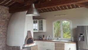 A kitchen with a brick wall, wooden beams, a hanging light, a window with a view, and a built-in oven. - Villa with sea view, pets welcome - 12 guests (Bormes-les-Mimosas)