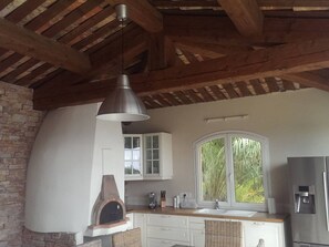A kitchen with a brick wall, wooden beams, a hanging light, a window with a view, and a built-in oven. - Villa with sea view, pets welcome - 12 guests (Bormes-les-Mimosas)