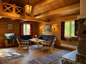 A log cabin interior with a sofa, chairs, a table, and a television.