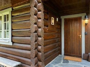 A log cabin with a stone porch, a wooden door, and a window with a white frame.