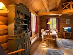 A cozy log cabin interior with a dining table, chairs, a television, and a large cabinet.
