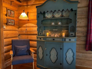 A log cabin interior with a blue cabinet, a chair, and a wall-mounted lamp.