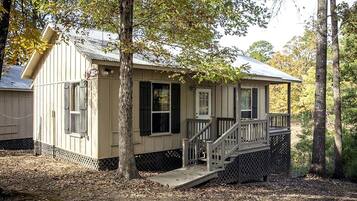 A small, single-story cabin with a porch, surrounded by trees.
