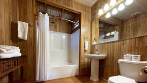 Ein Badezimmer mit Holzvertäfelung, einer Badewanne, einem Waschbecken und einer Toilette.