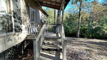 Une terrasse en bois qui mène à un porche abrité, offrant une vue sur une zone boisée.