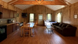 A spacious cabin with a wooden interior, a dining area, a sofa, and a television. - Charming Pondview Cabin with Resort Amenities near Zwolle, Louisiana (Zwolle)