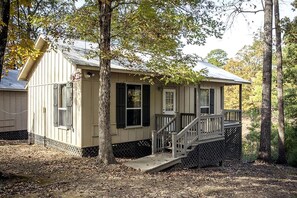 Eine kleine, eingeschossige Holzhütte mit Veranda, umgeben von Bäumen.