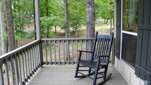 A porch with a rocking chair, wooden railing, and a view of trees. - Charming Pondview Cabin with Resort Amenities near Zwolle, Louisiana (Zwolle)