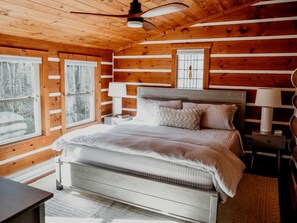 A wooden cabin bedroom with a bed, nightstands, a window, and a ceiling fan.